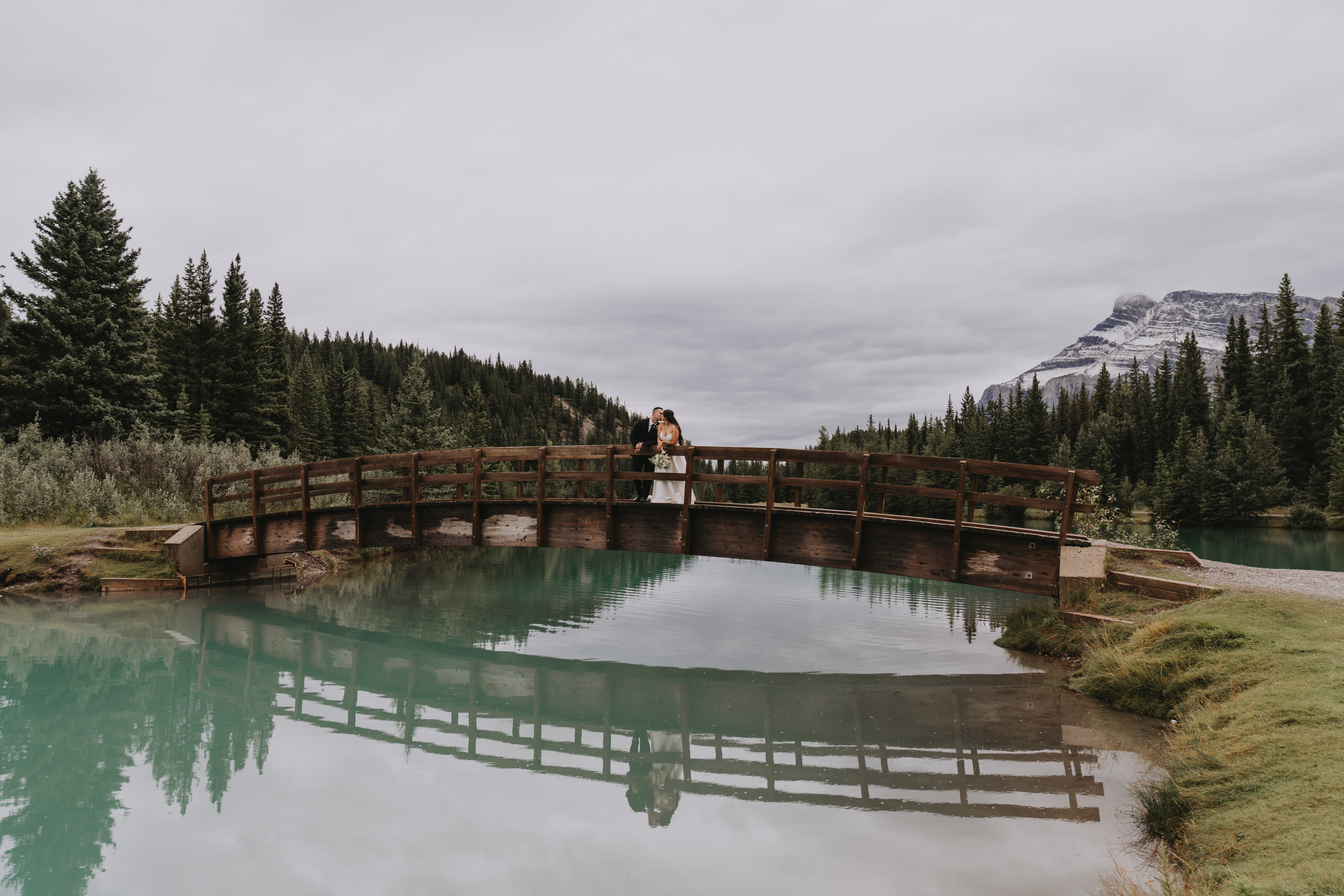 Bride and groom standing on a wooden bridge over turquoise water in Banff, Alberta.