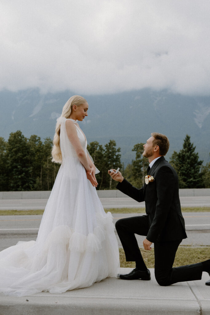 Groom proposing to bride on one knee with mountains in the background near Canmore.