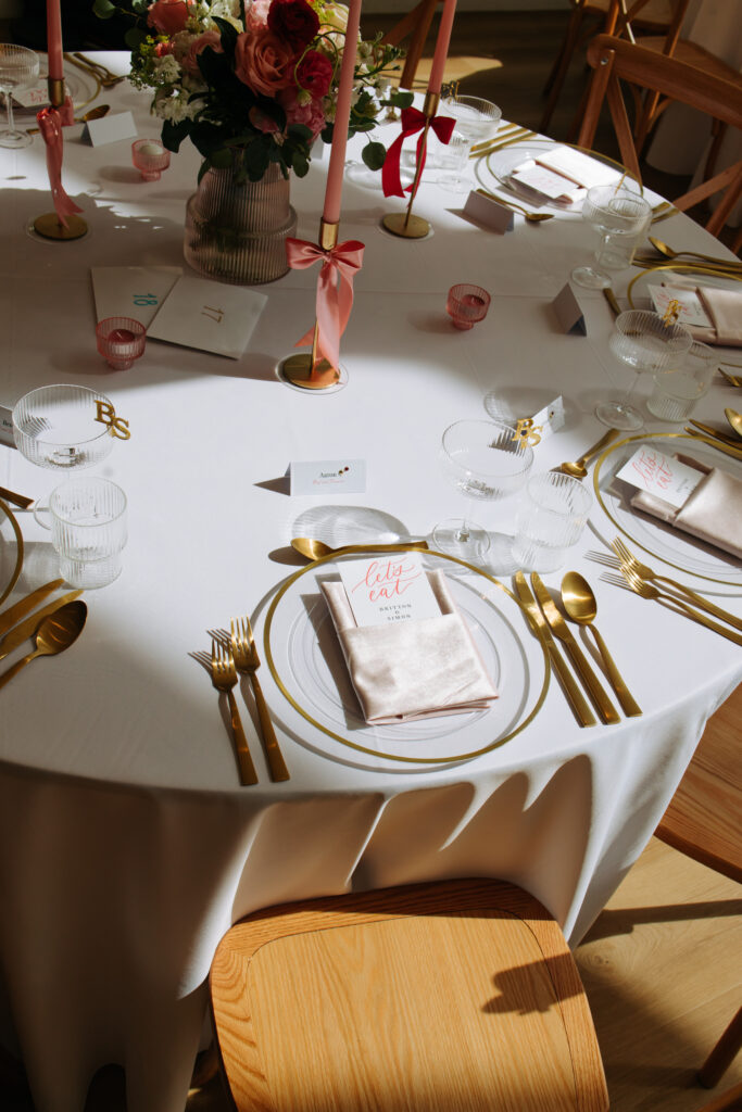 Elegant wedding place setting at The Gem featuring gold cutlery, blush linens, pink taper candles, and a floral centerpiece.
