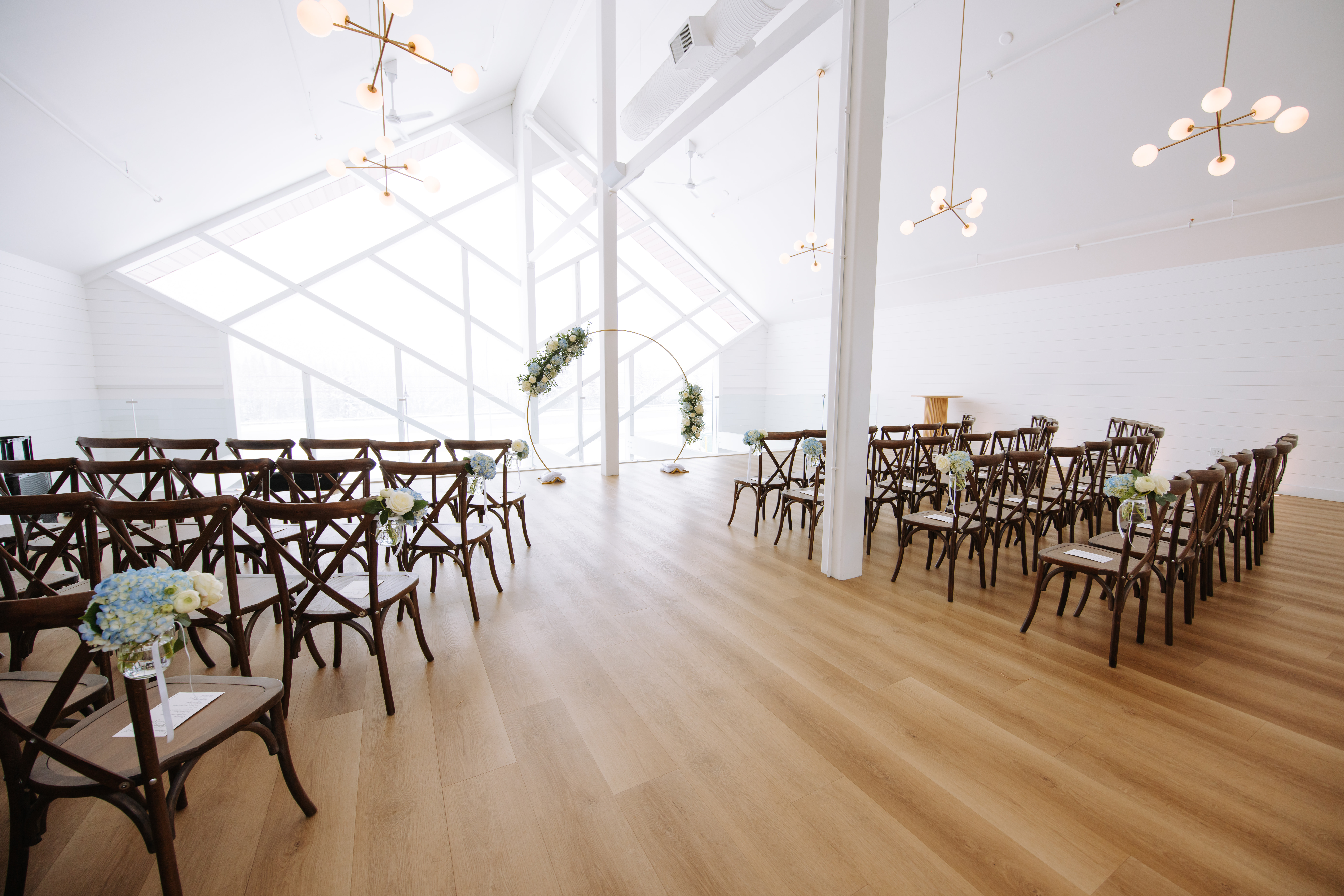 Modern indoor wedding ceremony setup at The Gem in Canmore with geometric windows and wooden chairs.