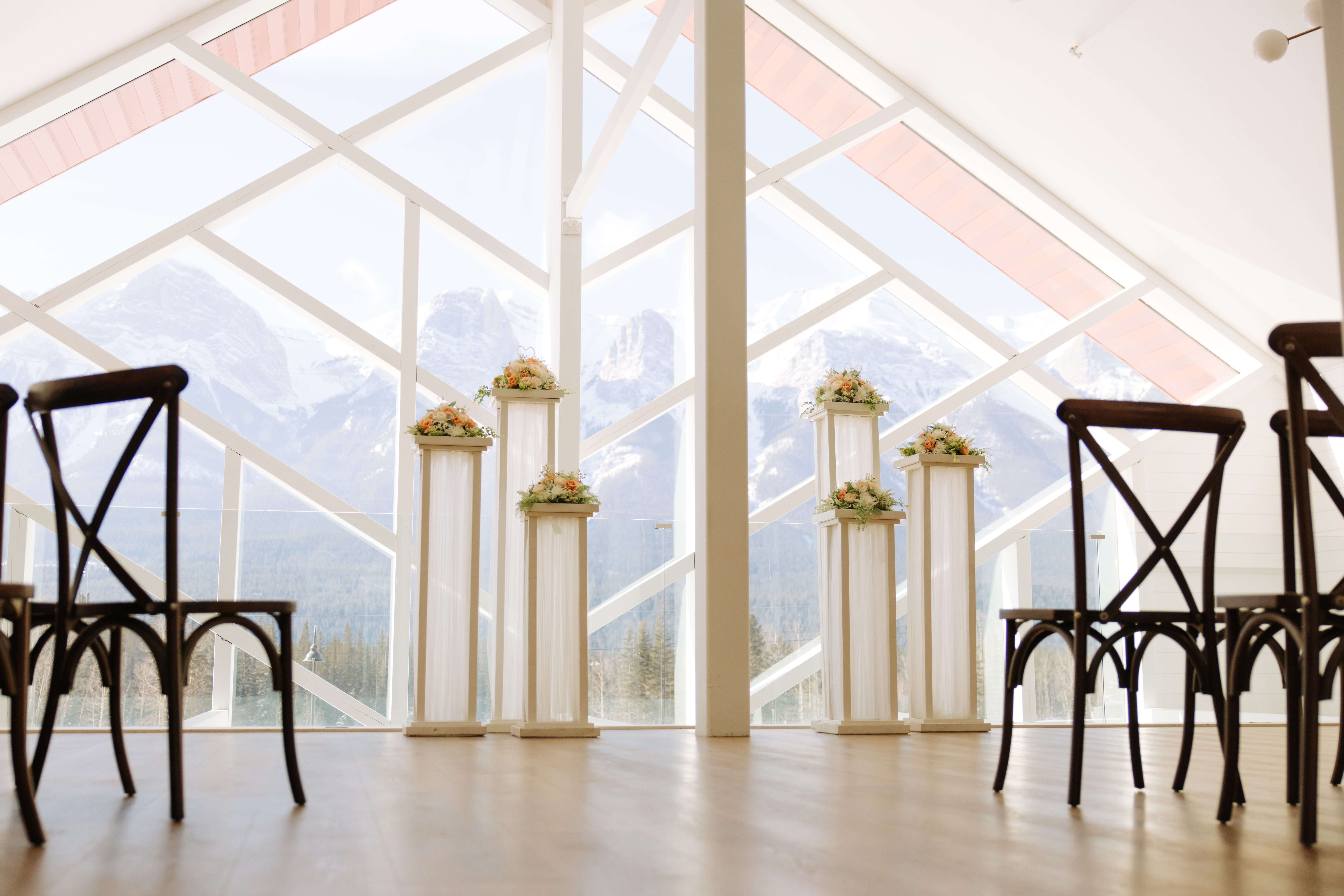 Indoor wedding ceremony setup at The Gem with pedestal florals and a full view of the Three Sisters mountains through large geometric windows.