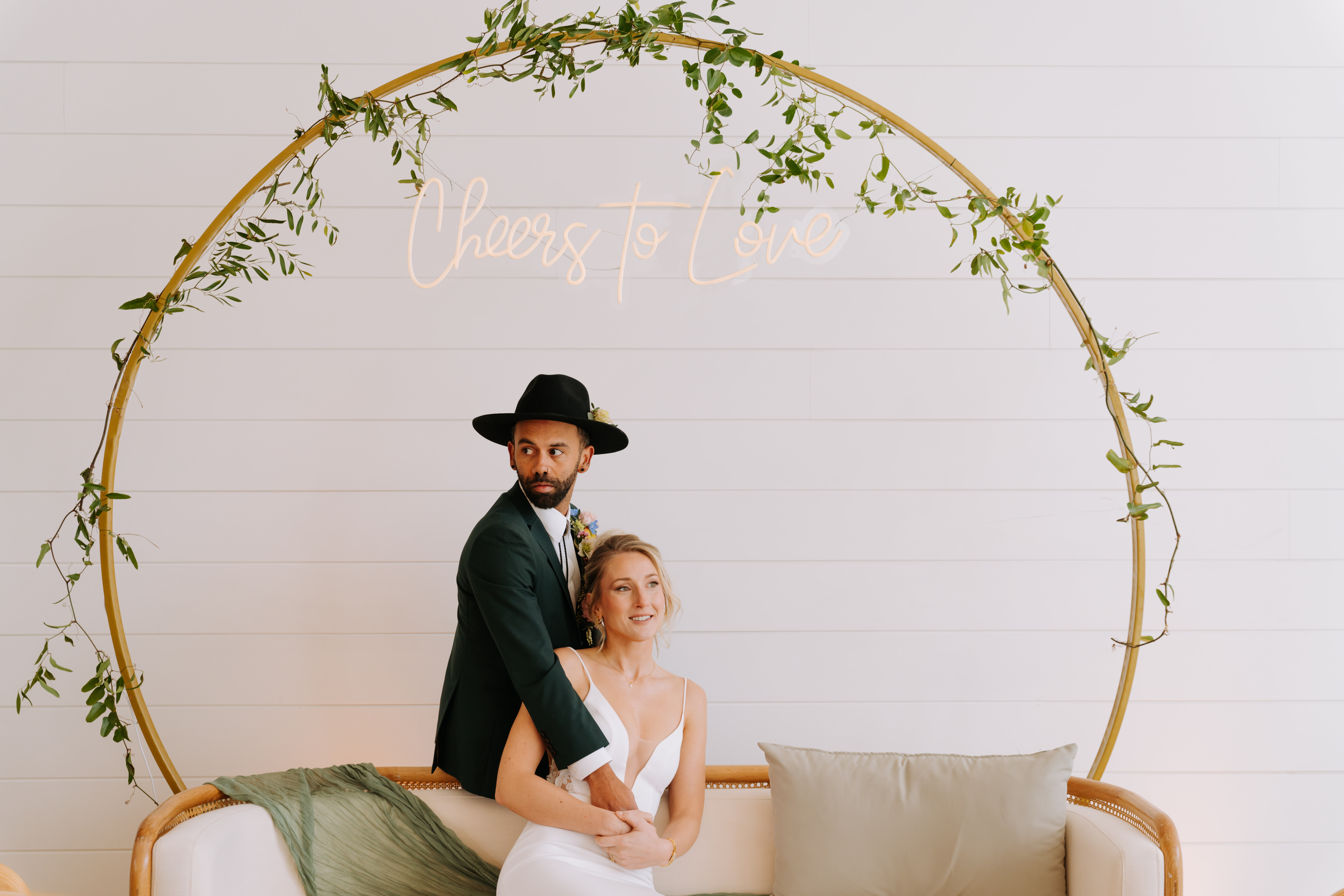 Bride and groom posing in front of a neon “Cheers to Love” sign on a modern lounge setup at The Gem in Canmore.