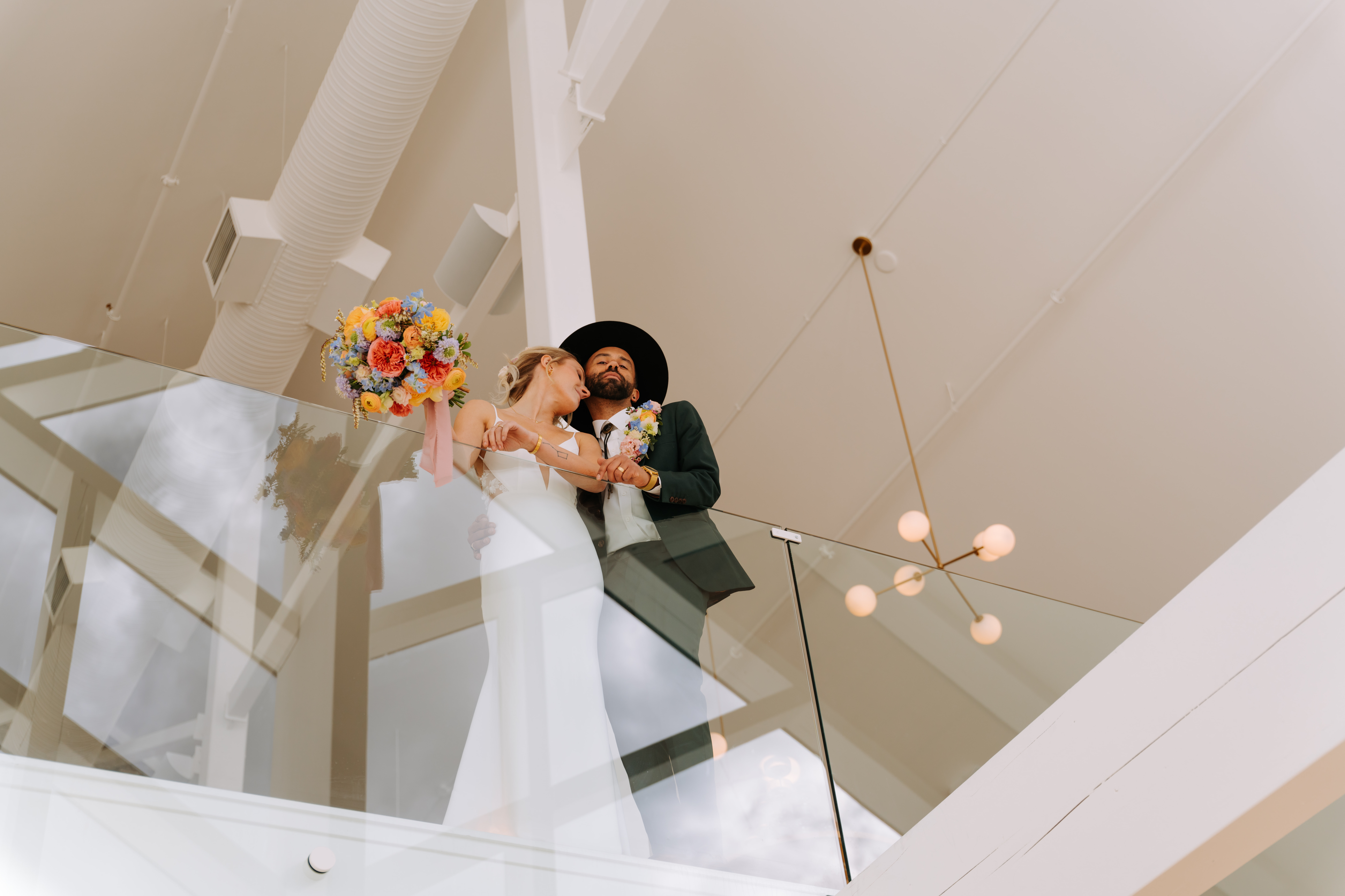 A bride and groom stand together on the mezzanine at The Gem, holding hands and a vibrant bouquet.