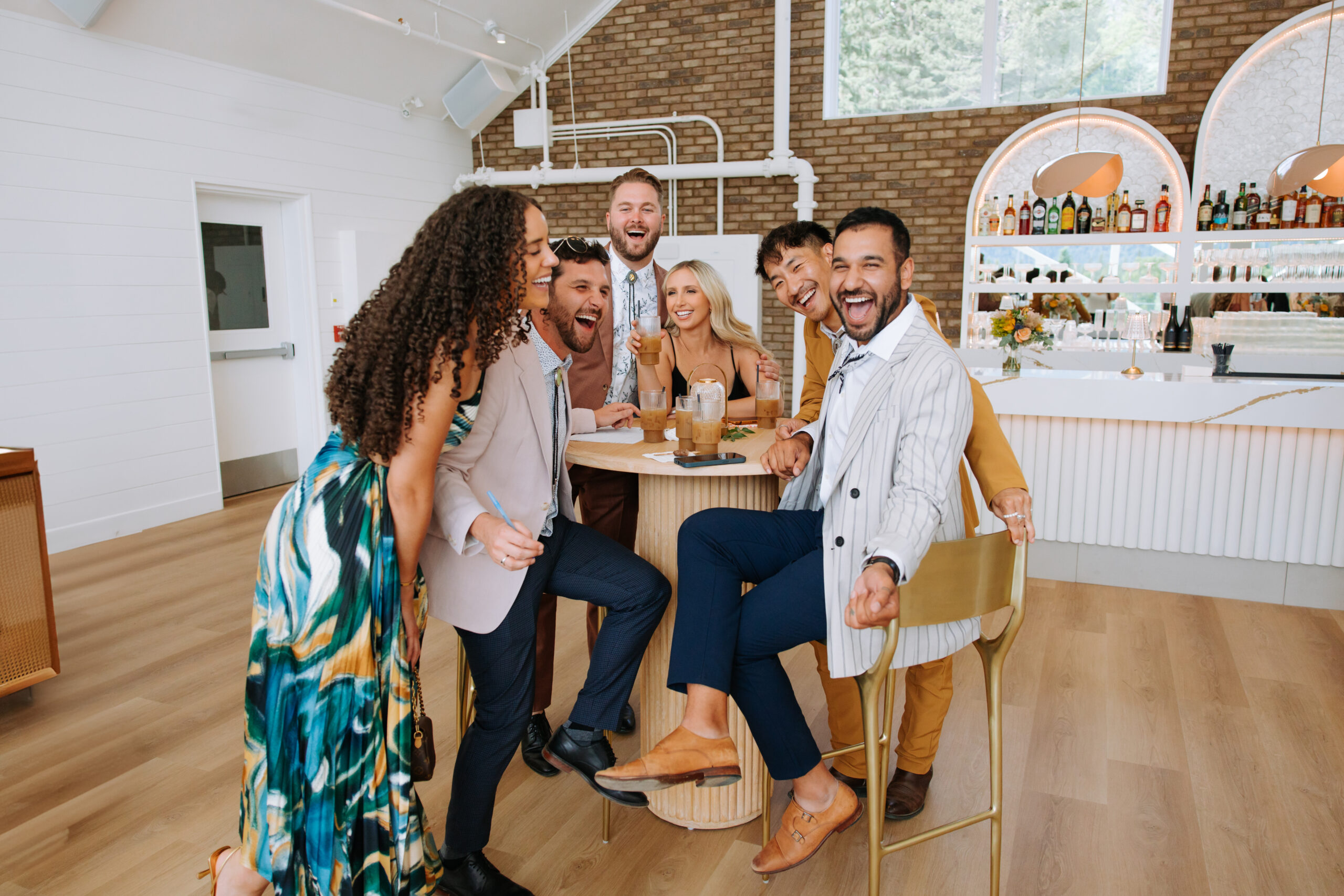 A stylish group of wedding guests laughing together at the bar inside The Gem, surrounded by cocktails and conversation.